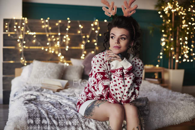 Young woman in christmas jumper sitting on bed — Stock Photo
