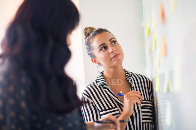 Young businesswomen looking at whiteboard adhesive notes — Stock Photo