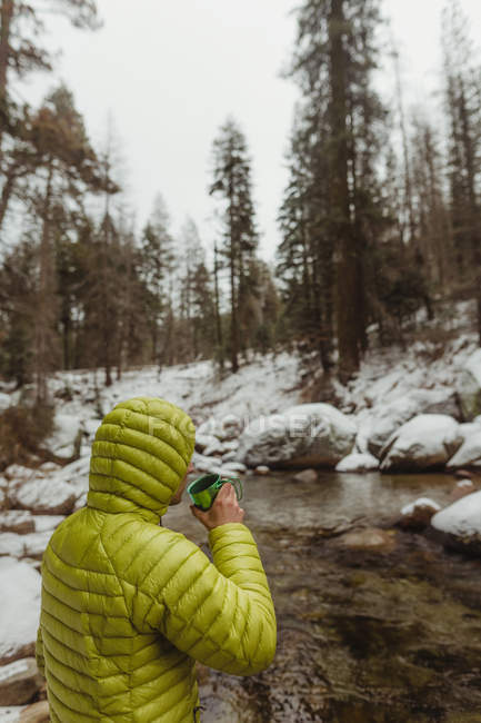 Male hiker drinking coffee near river in snowy Sequoia National Park, California, USA — Stock Photo