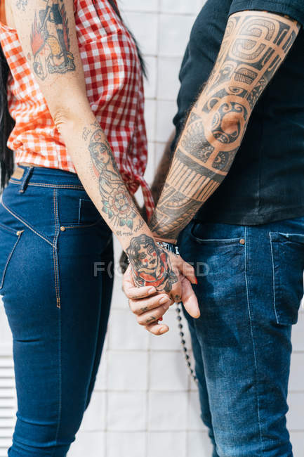 Maduro tatuado hipster pareja cogido de la mano, sección media - foto de stock