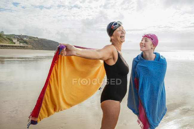Madre e hija de pie en la playa con chales - foto de stock
