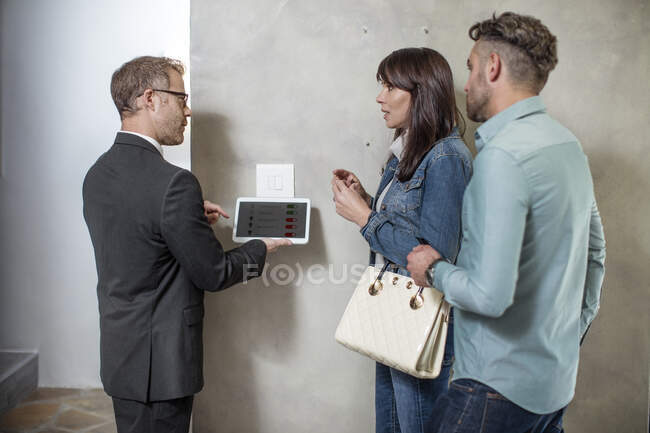Estate agent standing with couple, using digital tablet to demonstrate technology in new home — Stock Photo
