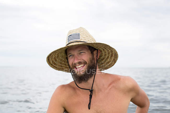 Ritratto di uomo sorridente che indossa cappello di paglia contro l'acqua — Foto stock