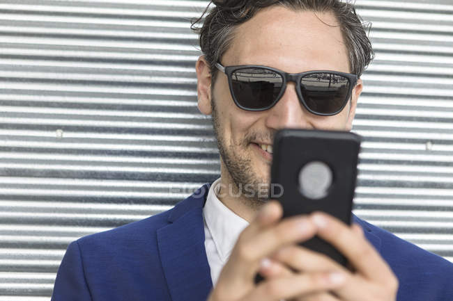 Young businessman in sunglasses looking at smartphone — Stock Photo