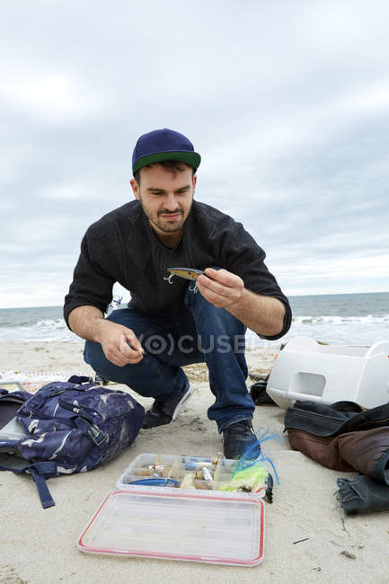 Фішер, дивлячись на гачок при crouching на пляжі — стокове фото