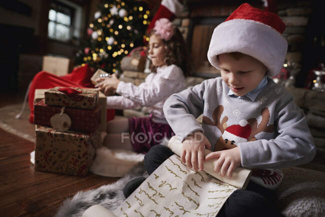 Joven chica y chico clasificación regalos de Navidad, joven chico lista rodante - foto de stock