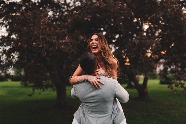 Jovem homem levantando namorada no parque ao anoitecer — Fotografia de Stock