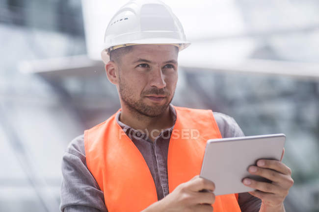 Hombre con sombrero duro y chaqueta de alta visibilidad usando tableta digital - foto de stock