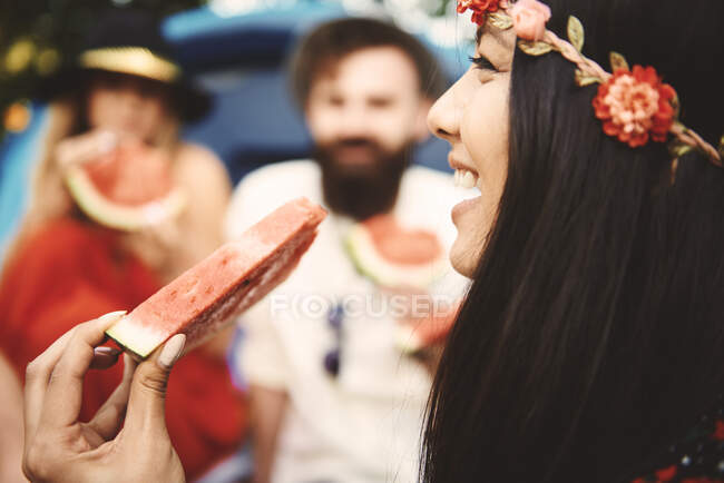 Joven mujer boho comiendo rodaja de melón en el festival - foto de stock