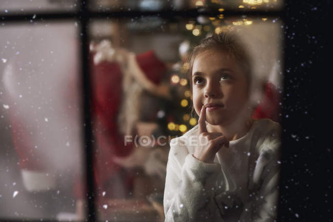 Молодая девушка смотрит в окно, пока Санта оставляет подарки возле дерева — стоковое фото