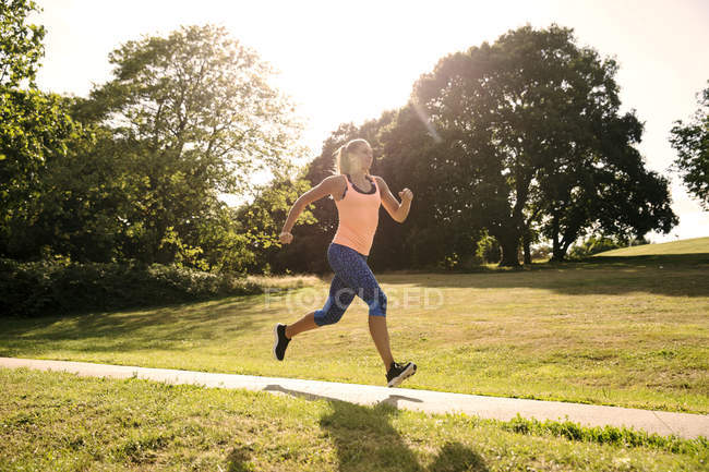 Молода жінка біжить вздовж паркової доріжки на сонячному світлі — стокове фото