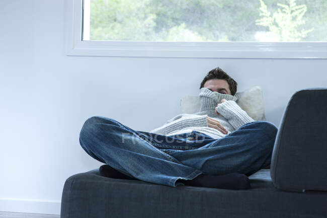 Man reclining on sofa peering from polo neck sweater — Stock Photo