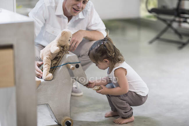Pai e bebê menina olhando para o cavalo de balanço — Fotografia de Stock