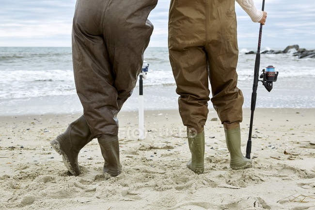 Jeune couple dans les échassiers de pêche sur la plage — Photo de stock