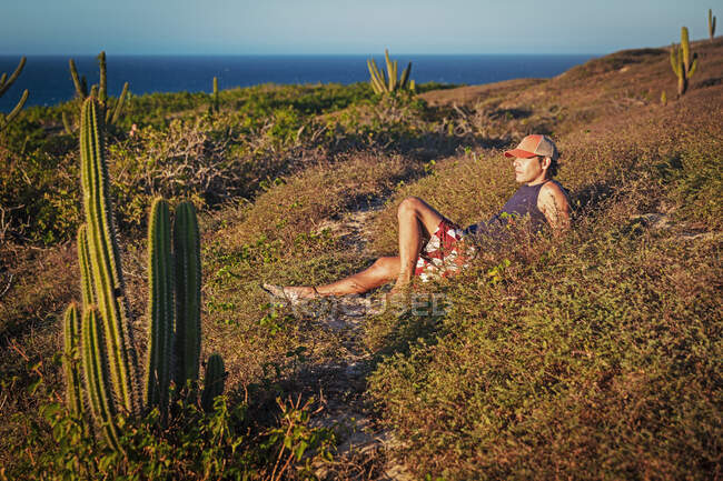 Hombre relajándose en la hierba, rodeado de cactus, Parque Nacional Jericoacoara, Ceara, Brasil - foto de stock
