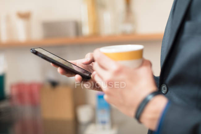Mani di uomo d'affari in possesso di tazza di caffè e smartphone — Foto stock
