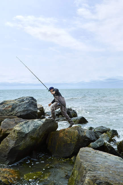 Junger männlicher Seefischer tritt über Strandfelsen — Stockfoto