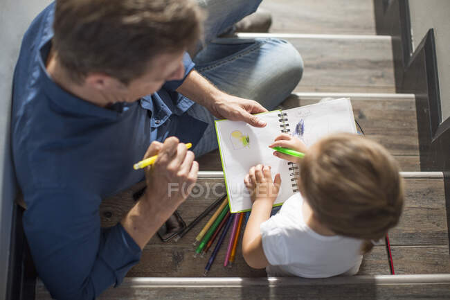High angle view of father and daughter on stairs drawing in notebook — Stock Photo