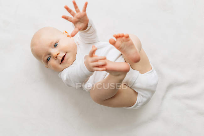 Sorrindo Bebê menina deitada nas costas, braço e pernas levantadas, olhando para a câmera — Fotografia de Stock