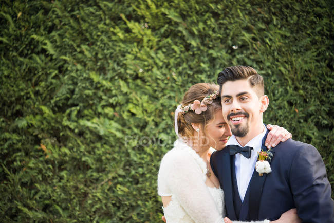 Portrait of bride and bridegroom with hedge at background — Stock Photo