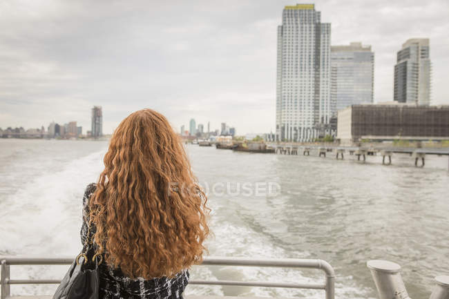 Задній вид довгі червоні волосся жінка на поромі палубі, дивлячись горизонт Нью-Йорк, США — стокове фото