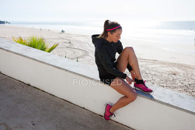 Junge Frau am Strand zieht Trainingsschuhe an, carcavelos, lisboa, portugal, europa — Stockfoto