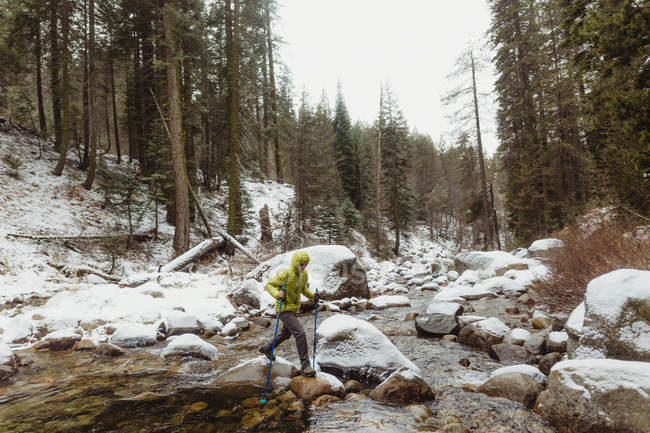 Мужчина-турист, переступающий породу реки в снежном Национальном парке Секвойя, Калифорния, США — стоковое фото