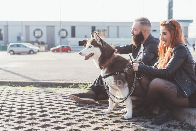 Jeune couple assis avec chien en plein air — Photo de stock