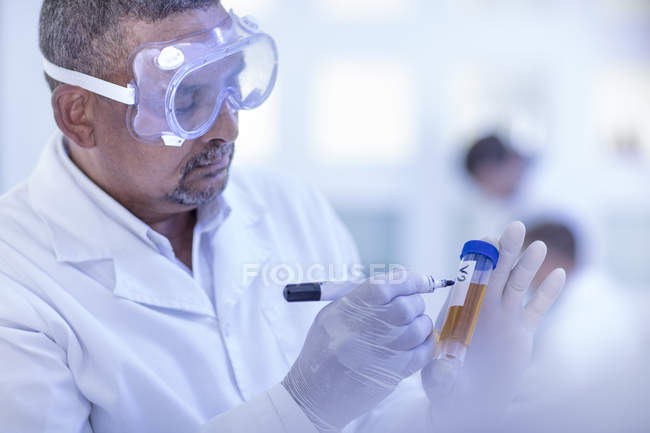 Trabajador de laboratorio escribiendo detalles sobre tubo de ensayo - foto de stock