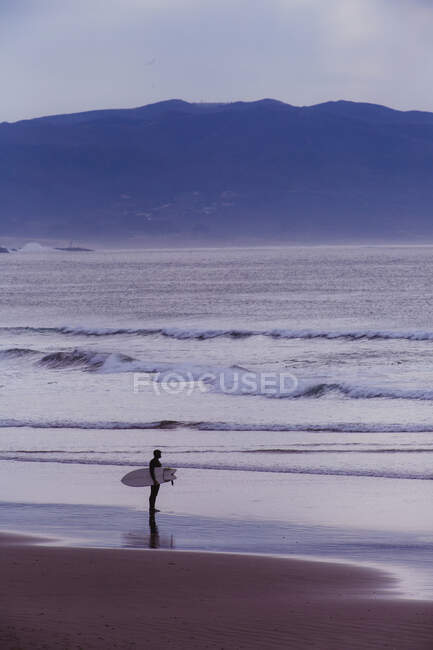 Joven surfista masculino mirando sobre el mar, Morro Bay, California, EE.UU. - foto de stock