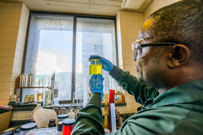 Labortechniker betrachtet Becher mit gelbem Biokraftstoff im Labor einer Biokraftstoffanlage — Stockfoto