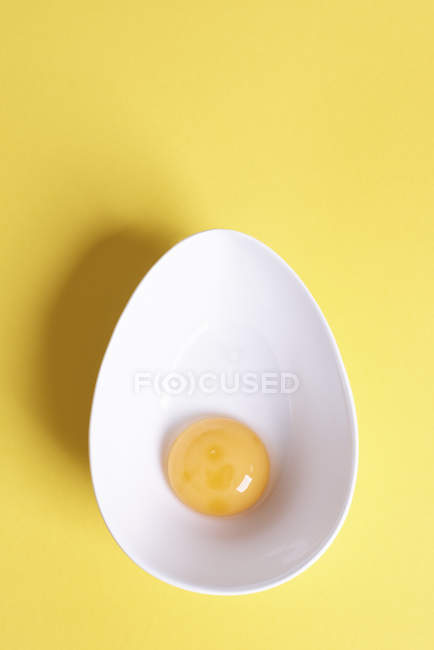 Overhead view of egg yolk in oval bowl on yellow background — Stock Photo