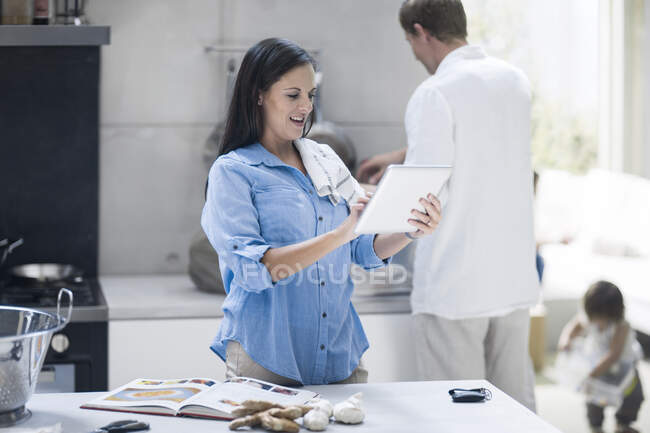Husband and wife making preparations in kitchen, toddler girl in background — Stock Photo