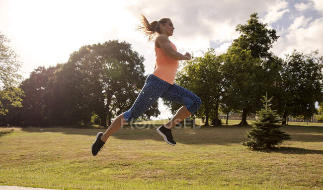 Молода жінка стрибає середнє повітря і тренується в парку — стокове фото