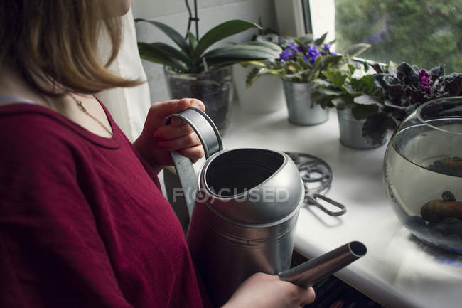 Femme arrosant des plantes en pot sur le rebord de la fenêtre — Photo de stock