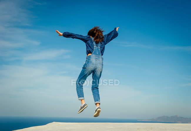 Вид сзади на девушку, прыгающую в воздухе, Санторини, Кикладес, Греция — стоковое фото
