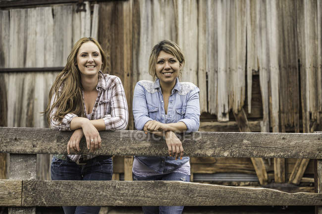 Портрет двух молодых женщин, прислонившихся к забору, улыбающихся — стоковое фото