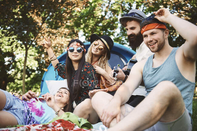 Cinco amigos adultos jóvenes tocando la guitarra acústica mientras acampan en el festival - foto de stock