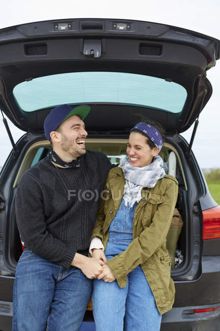 Young couple sitting and laughing in open car trunk — Stock Photo