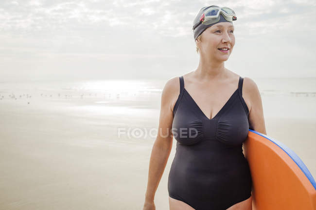 Mujer con tabla de surf mirando hacia la playa - foto de stock
