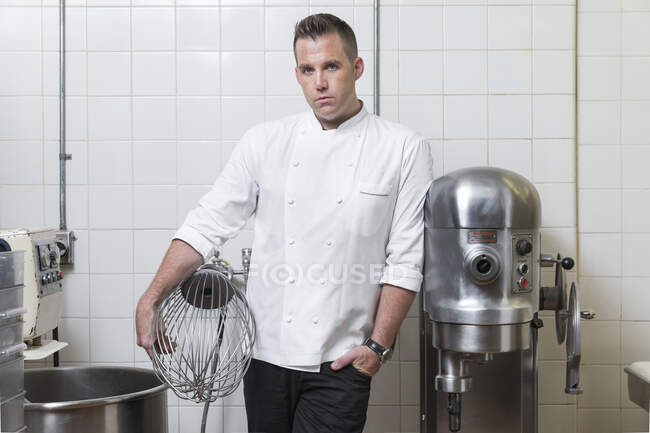 Портрет кондитера, держащего промышленный венчик на кухне — стоковое фото