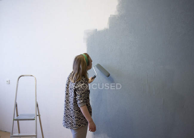Mujer joven aplicando pintura gris a la pared interior en casa - foto de stock