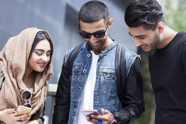 Drei Freunde auf der Straße schauen aufs Smartphone — Stockfoto