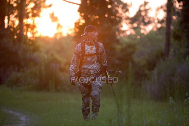 Mature man carrying crossbow and walking on grass — Stock Photo