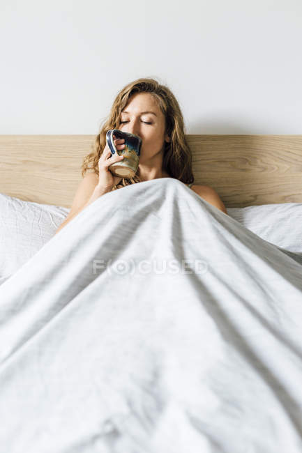 Jovem mulher bebendo café na cama — Fotografia de Stock