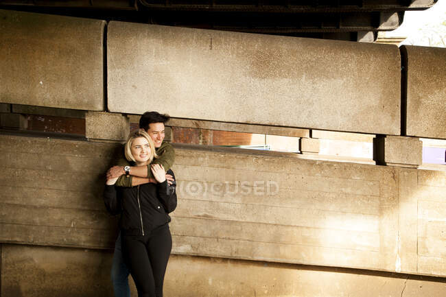 Молода пара, стоячи під мостом, обіймає — стокове фото