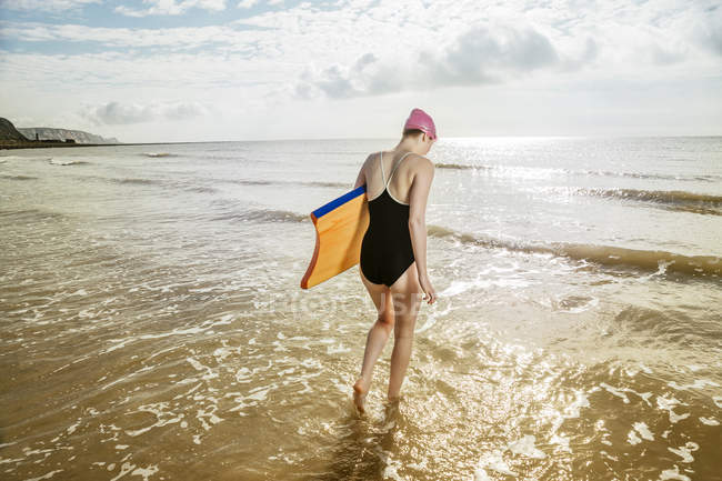 Giovane donna che porta la tavola da surf in mare — Foto stock