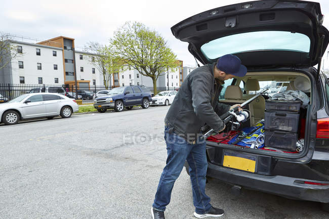 Young man packing fishing rod into car trunk — Stock Photo