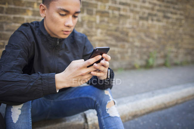 Молодой человек с помощью смартфона сидит на тротуаре — стоковое фото