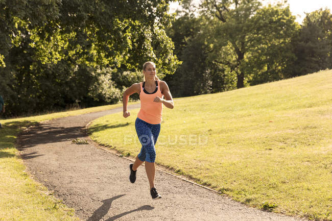 Jovem fêmea correndo ao longo do caminho do parque — Fotografia de Stock